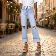 A pair of distressed straight leg flare jeans by Aapparella displayed on a hanger, showcasing the ripped details and relaxed fit.