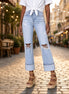 A pair of distressed straight leg flare jeans by Aapparella displayed on a hanger, showcasing the ripped details and relaxed fit.
