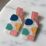 Avenue Zoe rectangular abstract dangle earrings with geometric design and mixed metal finishes hanging on display