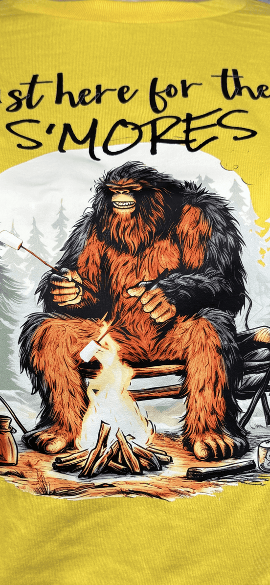 Squatchin’ Country Bigfoot roasting marshmallows graphic T-shirt, casual outdoor wear featuring a Bigfoot silhouette with marshmallow roasting scene.