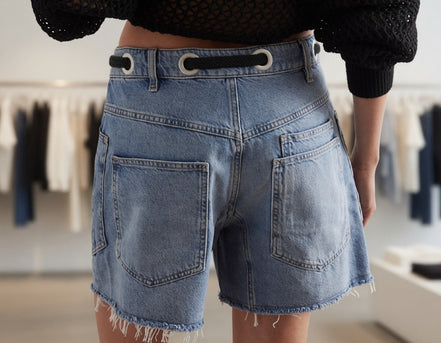Mccolin lace-up denim shorts featuring distressed details and a high-waisted fit, showcased on a model in a casual summer setting.