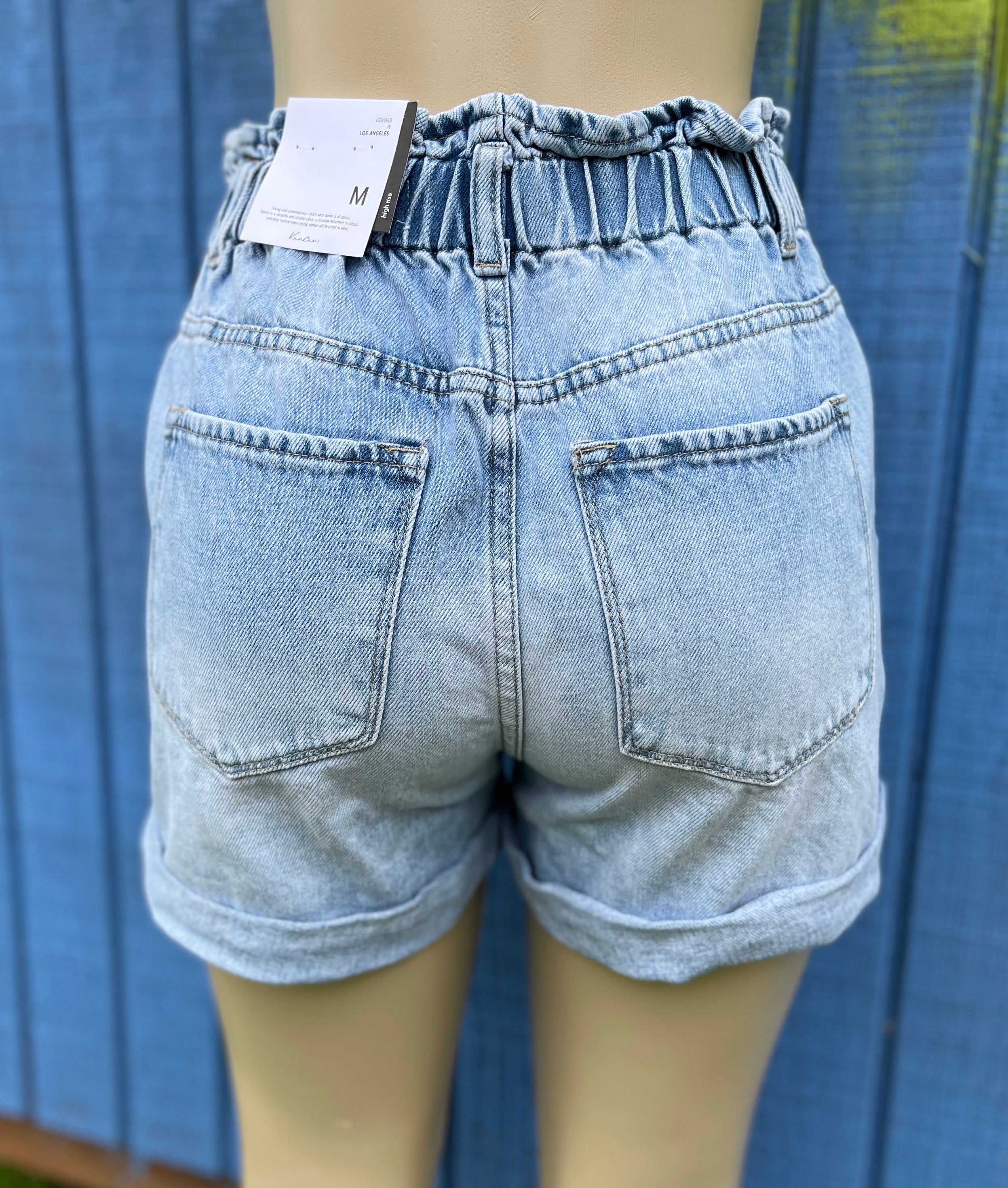 KanCan denim shorts with distressed details and frayed hem, styled on a model for a casual summer look.