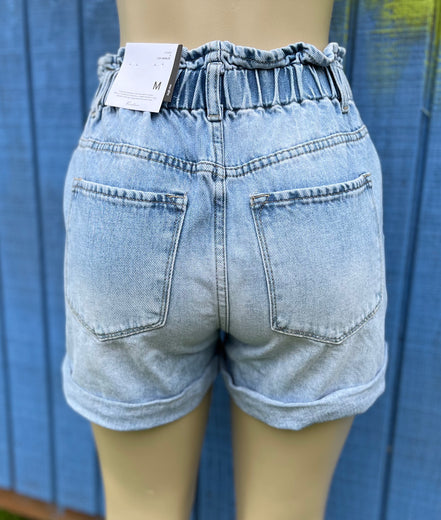 KanCan denim shorts with distressed details and frayed hem, styled on a model for a casual summer look.